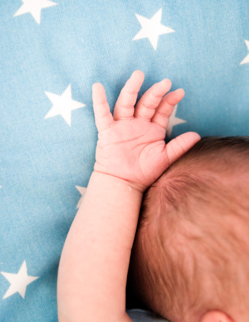 baby sleeping very relaxed with his arm raised above him