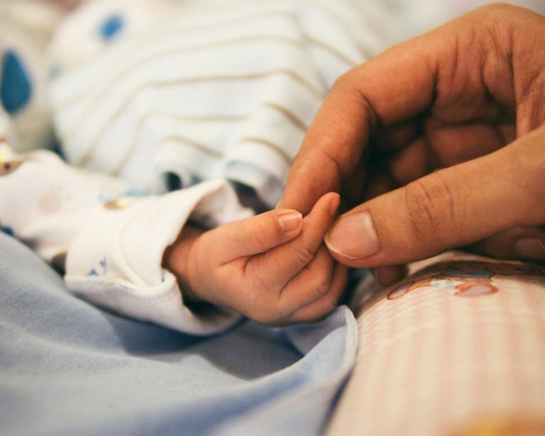 Mother hand gently holding the hand of a newborn sleeping baby