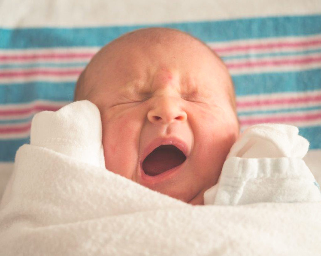 Newborn baby swaddled and yawning, ready for bed
